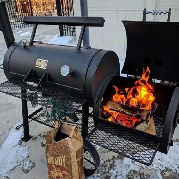 Offset smoker with a wood fire burning in the firebox, snow on the ground